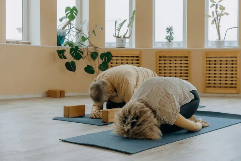 Two seniors practice Balasana or Child's Pose, a relaxing posture that may be used for arthritis relief and stress management