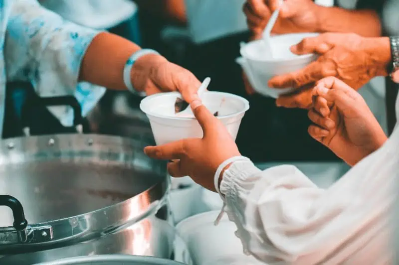 Close-up photo of hands passing a bowl of soup, an example of acts of service that serve as the foundation for karma yoga.