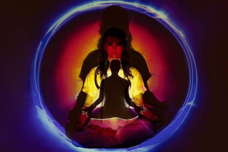 A woman meditates with projected small & large silhouettes & auras surrounding the figure as the three bodies and five koshas