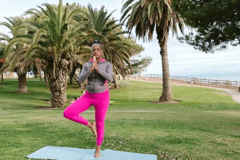 A woman stands in Tree Pose balancing on one leg with the other knee opening to the side; this pose is great for your joints!