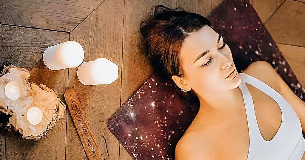 Feeling Sore After Yoga? Here's How to Soothe Your Muscles and Boost Recovery sore after yoga 18 this is a featured image for the article, it shows a woman laying on her yoga mat on wooden floor with candles next to her