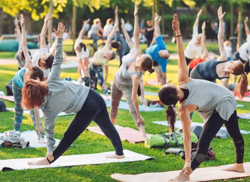 A diverse group of yoga students practice outdoors together, performing Triangle Pose, showing the popularity of the practice