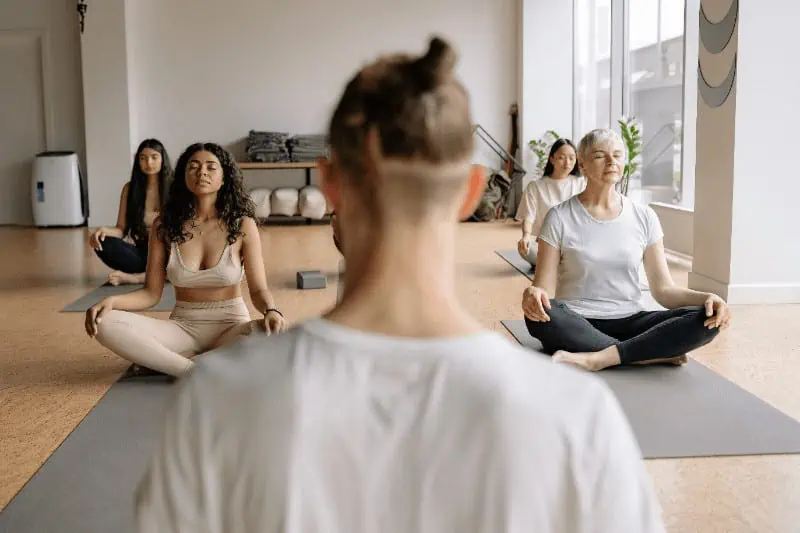 Yoga class lead by a yoga instructor where everyone is sitting on their yoga mat and practicing pranayama