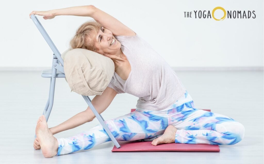 Comprehensive Guide to Yoga for Joint Pain yoga for joint pain 3 A person is practicing a supported side stretch using a chair on a yoga mat. Sitting with legs extended and slightly bent, they lean sideways, resting their head on a cushion placed on the chair for support. Their left arm stretches over their head to grasp the chair’s backrest, while the right arm rests gently on the floor. They wear a light-colored shirt and patterned leggings. The peaceful setup emphasizes gentle stretching for improved joint mobility and flexibility, making yoga more accessible for those seeking joint-friendly movement