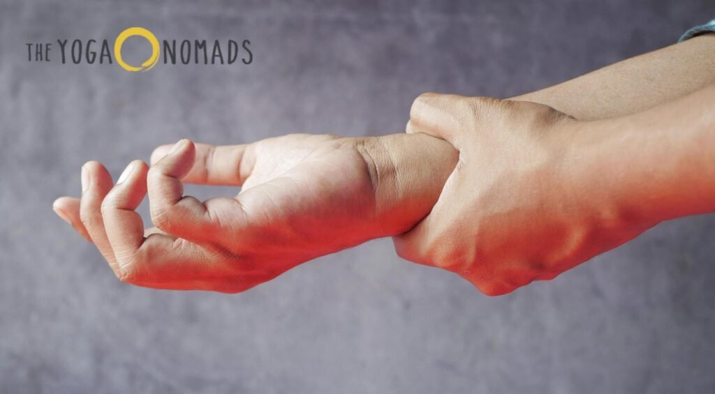 5 Top-Rated Online Yoga Classes for Joint Pain Management online yoga classes for joint pain 5 A person sits cross-legged on a yoga mat, gently clasping their wrist with one hand while forming a mudra with the other. They wear neutral-colored activewear, and the background is a plain gray surface. The branding 'THE YOGA NOMADS' appears in the top left corner, with the letter 'O' stylized as a yellow circle. This serene and focused posture emphasizes joint mindfulness and flexibility, making it a fitting representation for an article about the benefits of online yoga classes tailored to joint health.